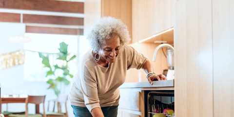 Photo of an older woman bending down to reach something in a dishwasher.