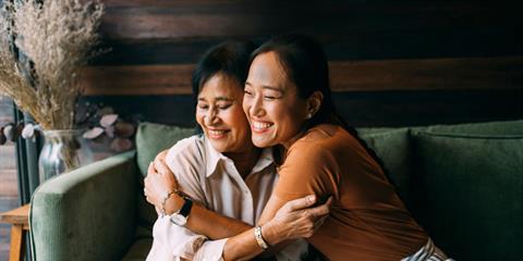 Photo of a woman hugging an older woman, both smiling, on a green couch.