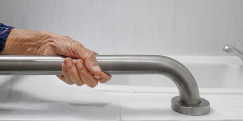 Photo of an older person holding onto a guardrail in the bathroom.