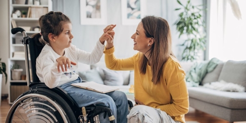 Photo of a child in a wheelchair high-fiving her caregiver.