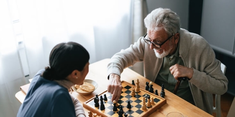 happy senior man playing chess with caregiver