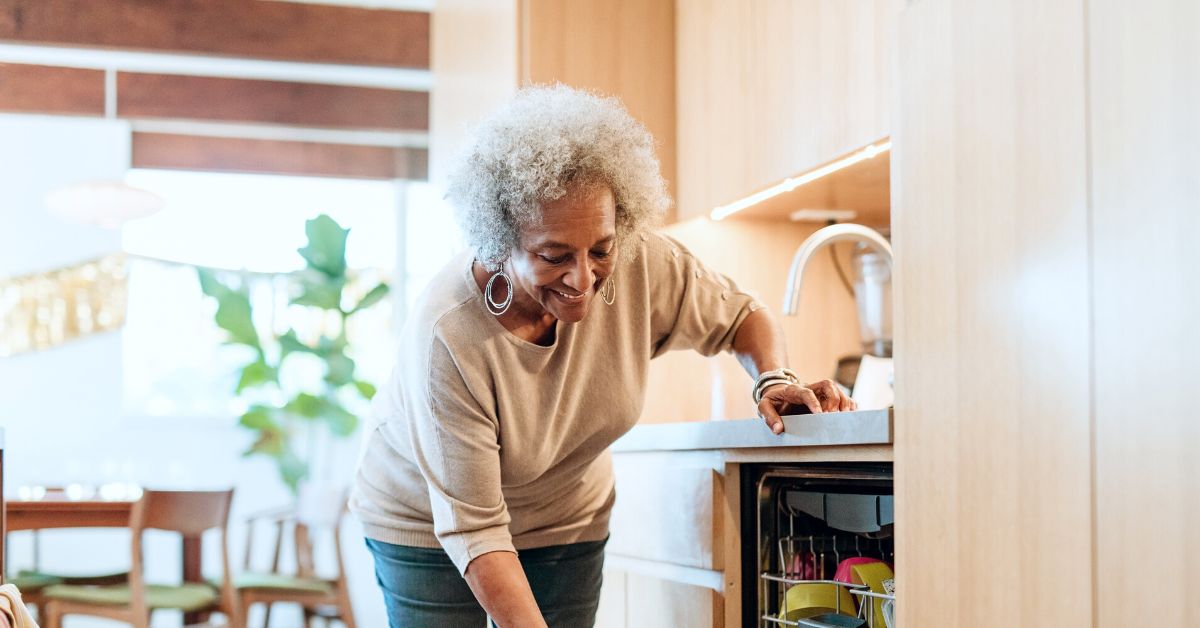 Photo of an older woman bending down to reach something in a dishwasher.
