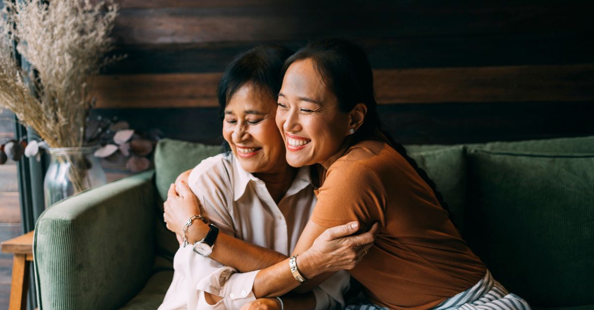 Photo of a woman hugging an older woman, both smiling, on a green couch.