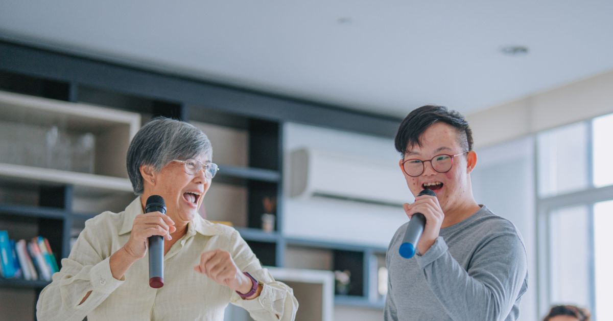 Photo of an older woman and younger man singing into microphones in their living room.