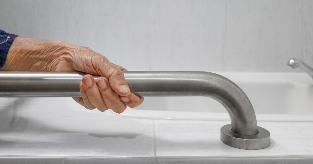 Photo of an older person holding onto a guardrail in the bathroom.