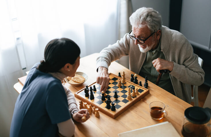 happy senior man playing chess with caregiver